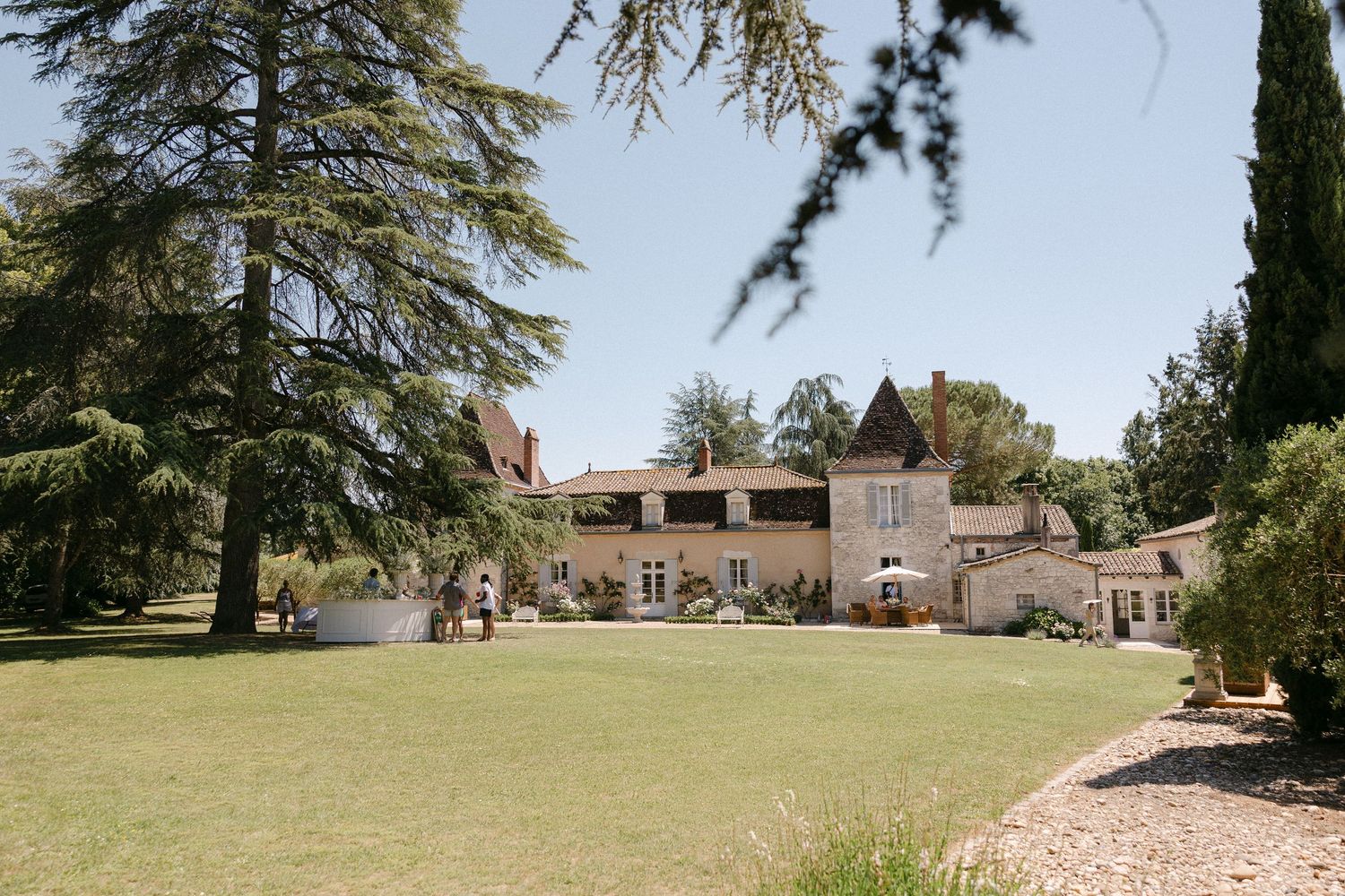 Stunning French chateau wedding venue surrounded by lush green lawns, tall cedar trees, and manicured gardens.