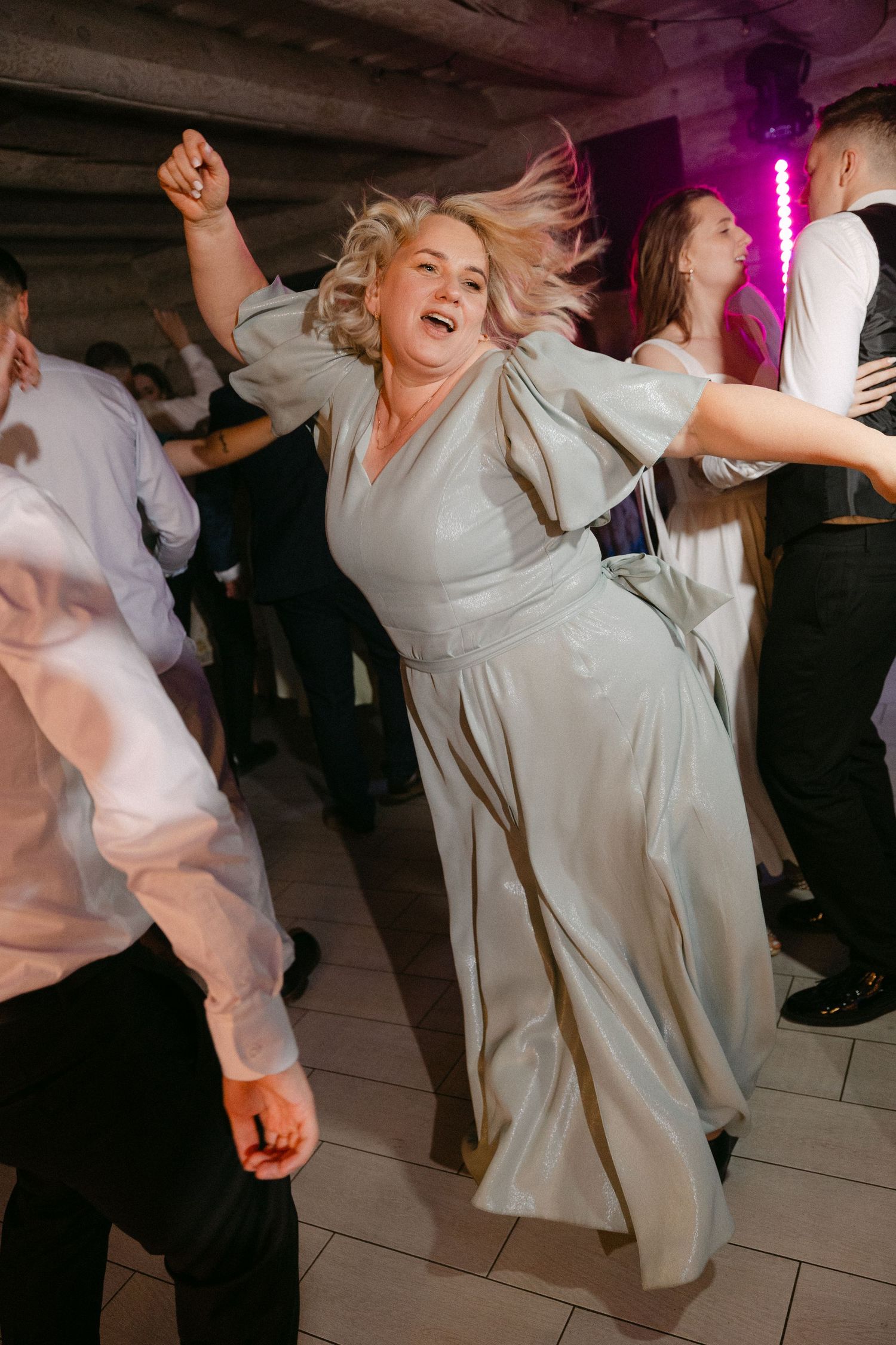 Wedding guest in sage green dress dances energetically with hair flying at lively reception party.