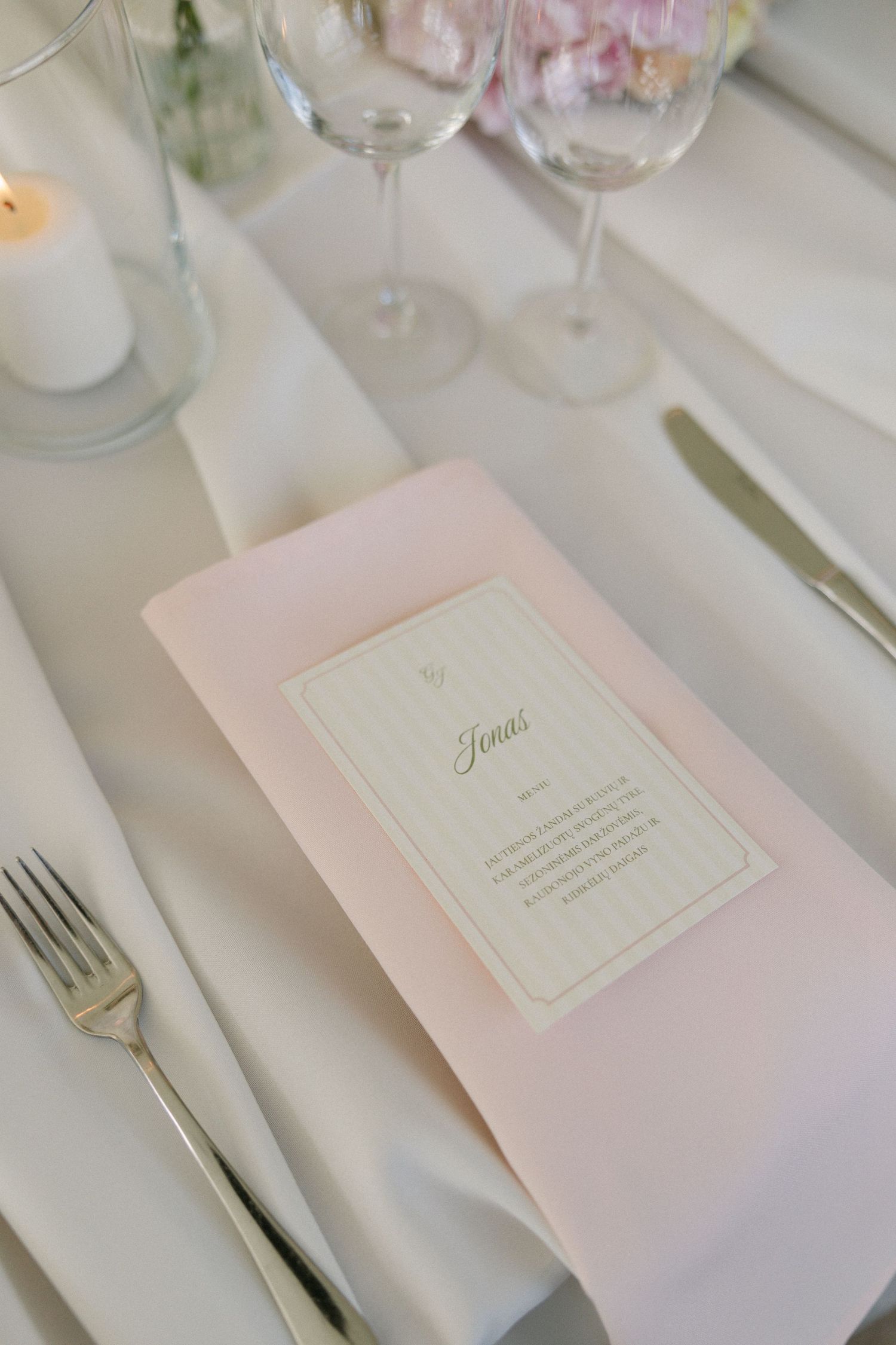 Elegant pink wedding reception place setting with menu card, fork, knife, candle, and wine glasses.
