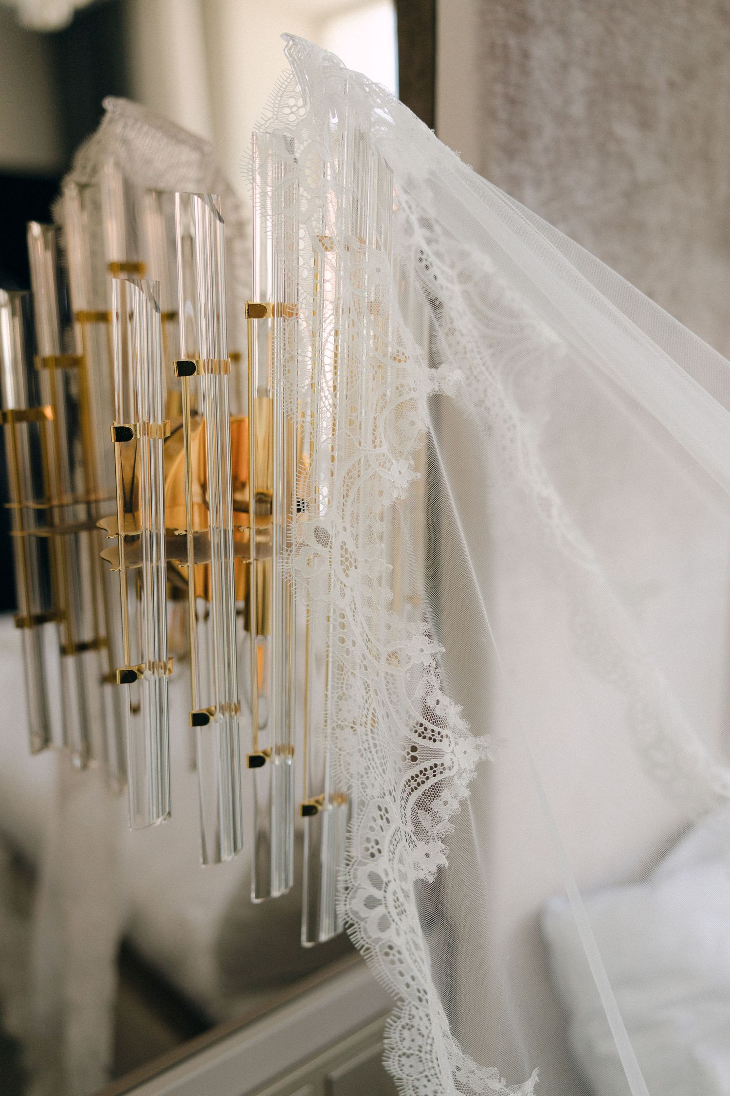 A delicate white lace wedding veil draped over a gold crystal wall sconce light fixture.