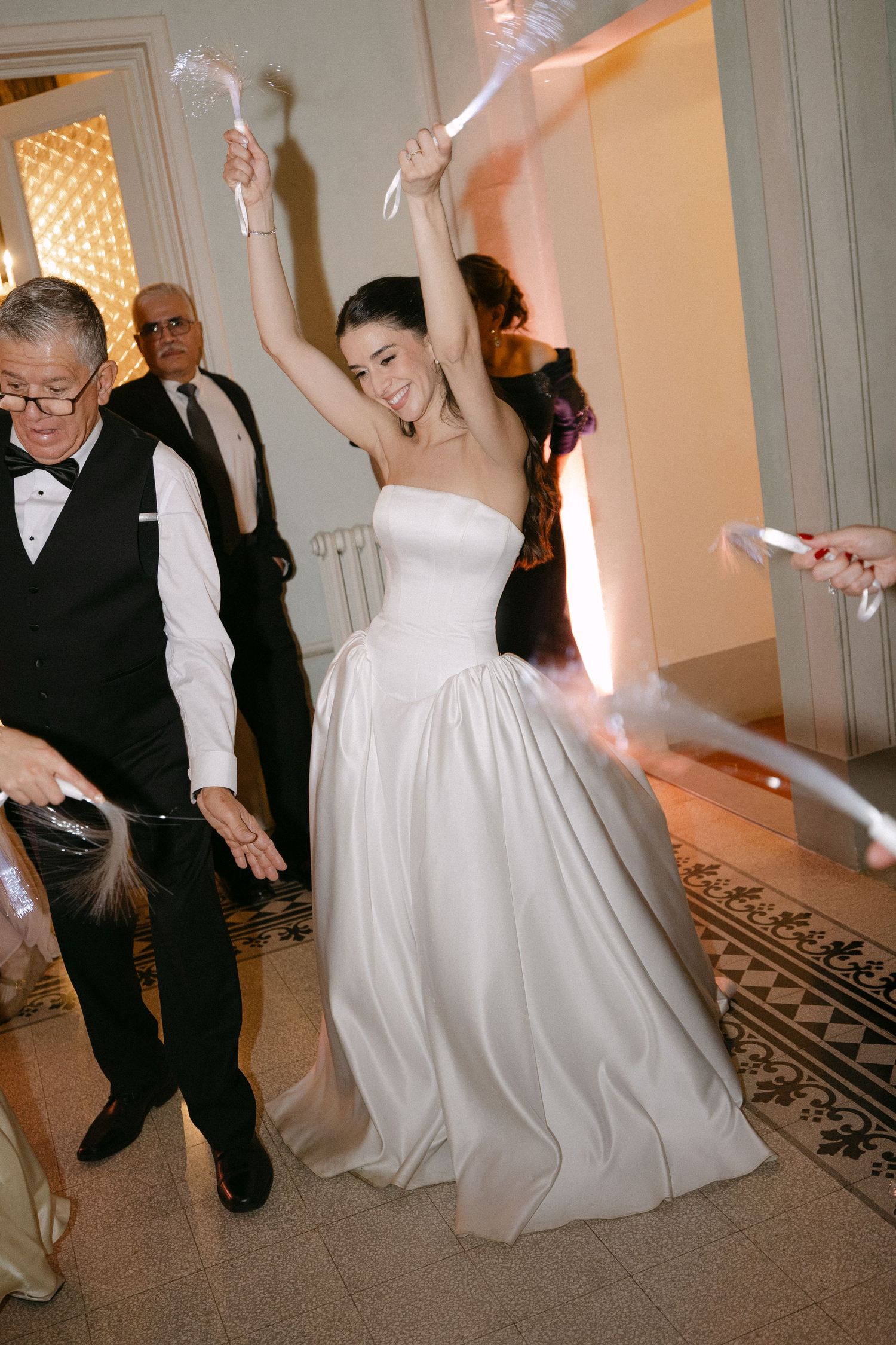 Radiant bride in strapless ball gown dances joyfully with sparklers at lively wedding reception.