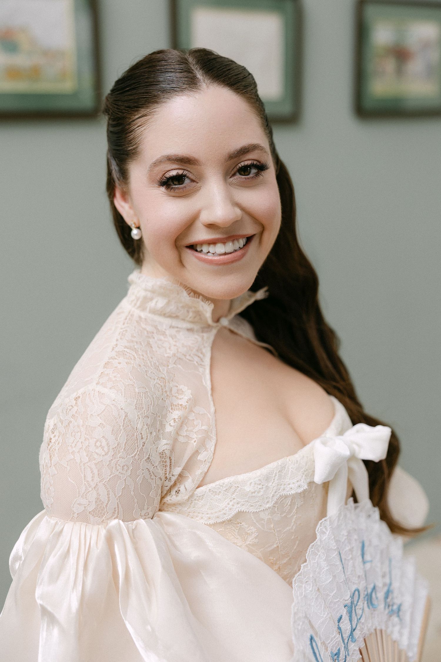 Smiling bride in vintage lace gown holding decorative fan on wedding day.