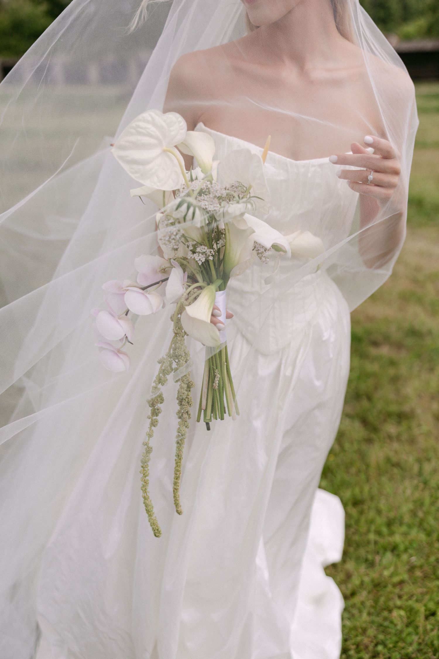 Close-up of bride in strapless white gown holding elegant white anthurium and calla lily bouquet with veil.