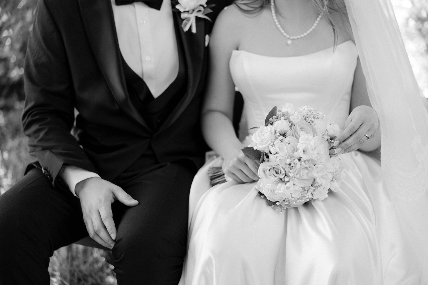 Black and white photo of bride holding white bouquet beside groom in tuxedo at wedding ceremony.