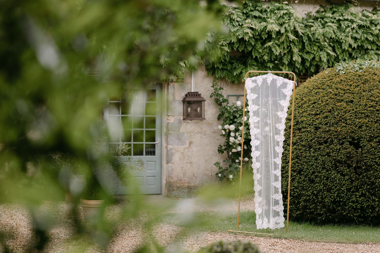 Elegant lace wedding arch stands beside manicured hedges at French chateau venue.