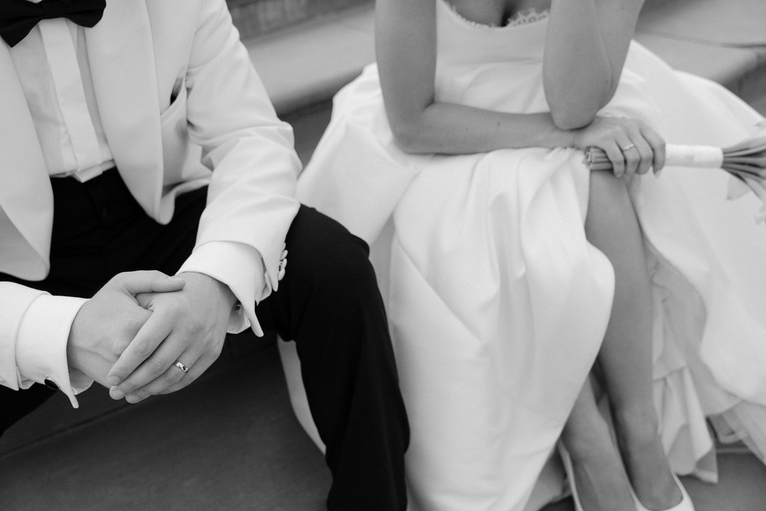 Close-up black and white photo of bride and groom holding hands during wedding reception.