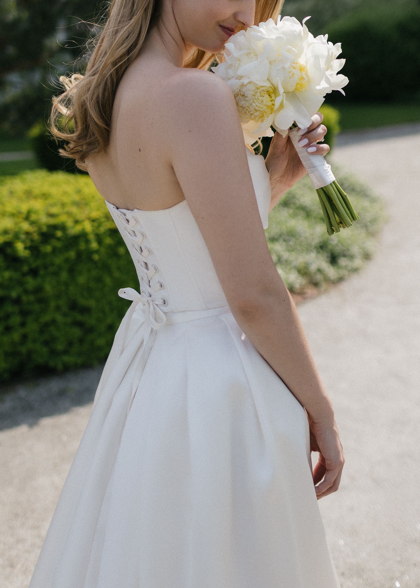 A bridal gown detail showing the corset back and white peony bouquet.