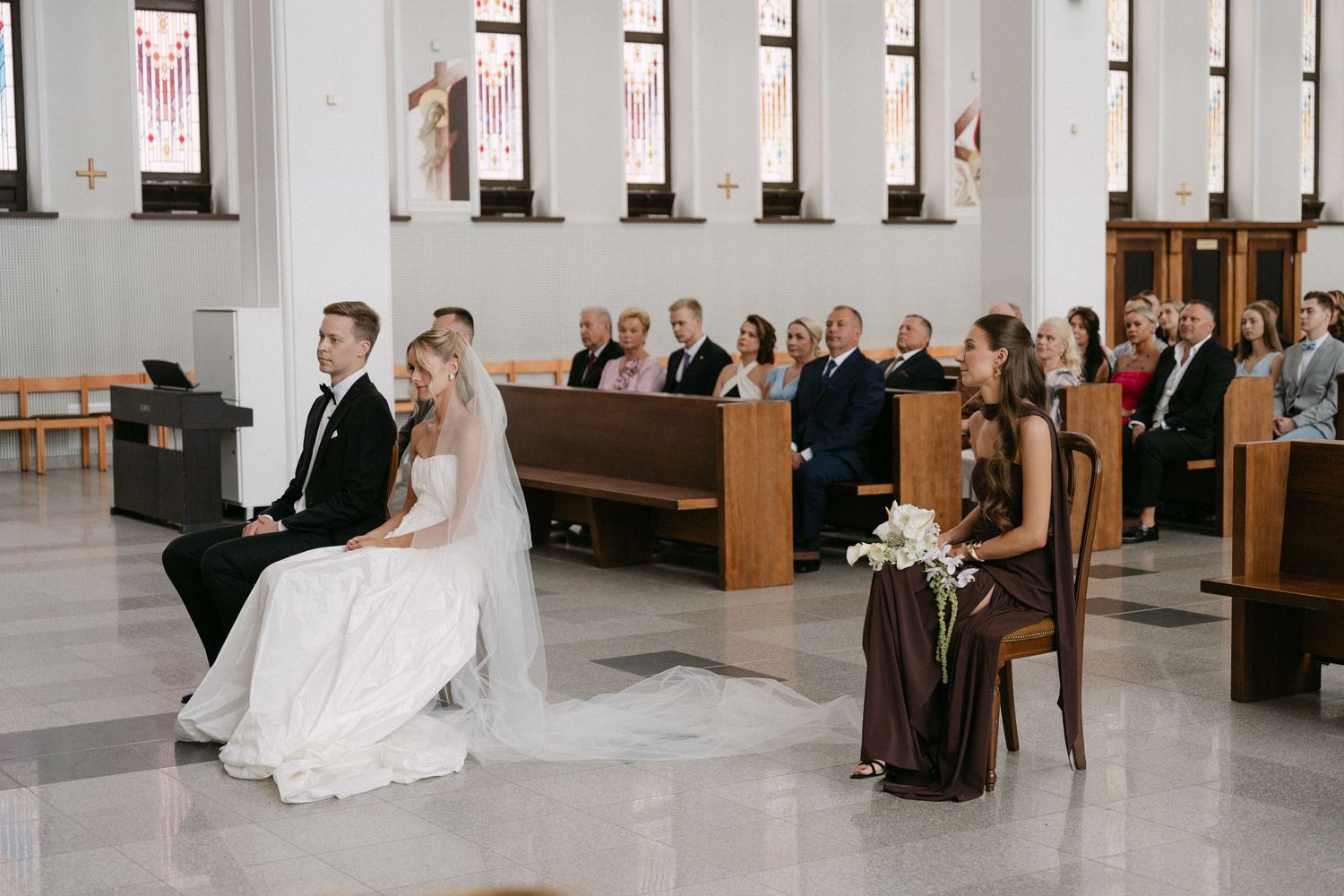 Bride and groom seated at the altar during a church wedding ceremony with guests in pews behind them.