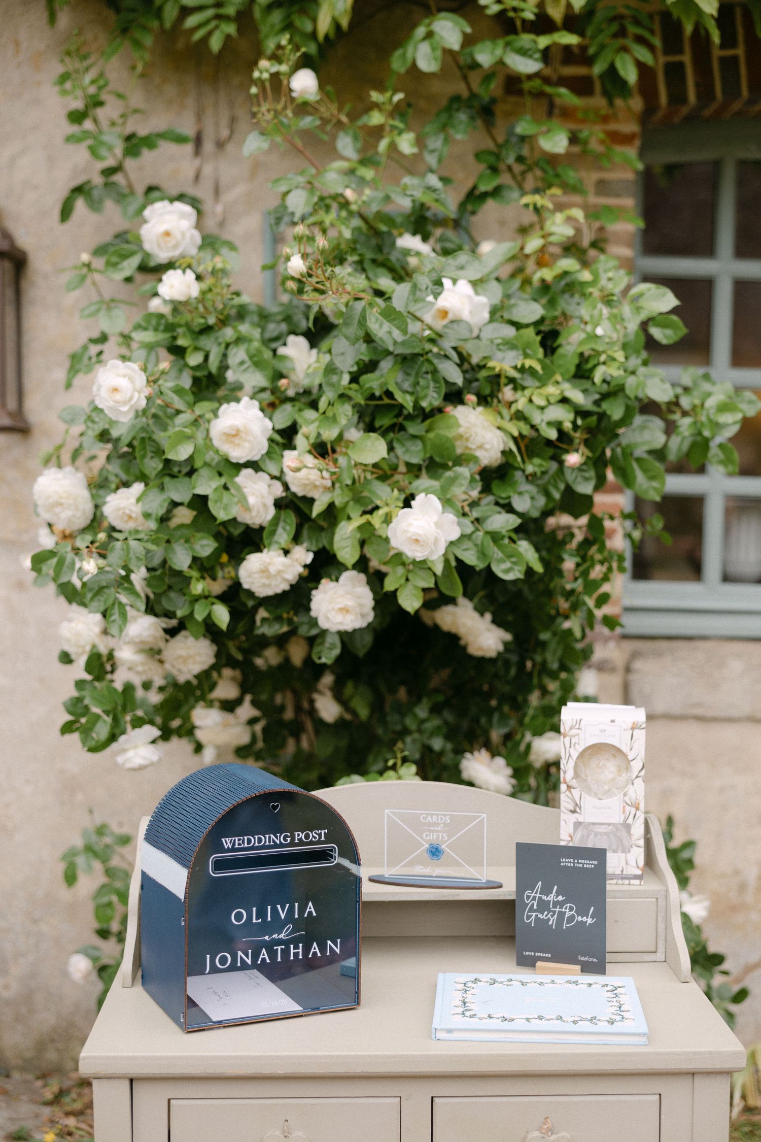 Wedding post box for Olivia and Jonathan displayed on table with white roses in background.