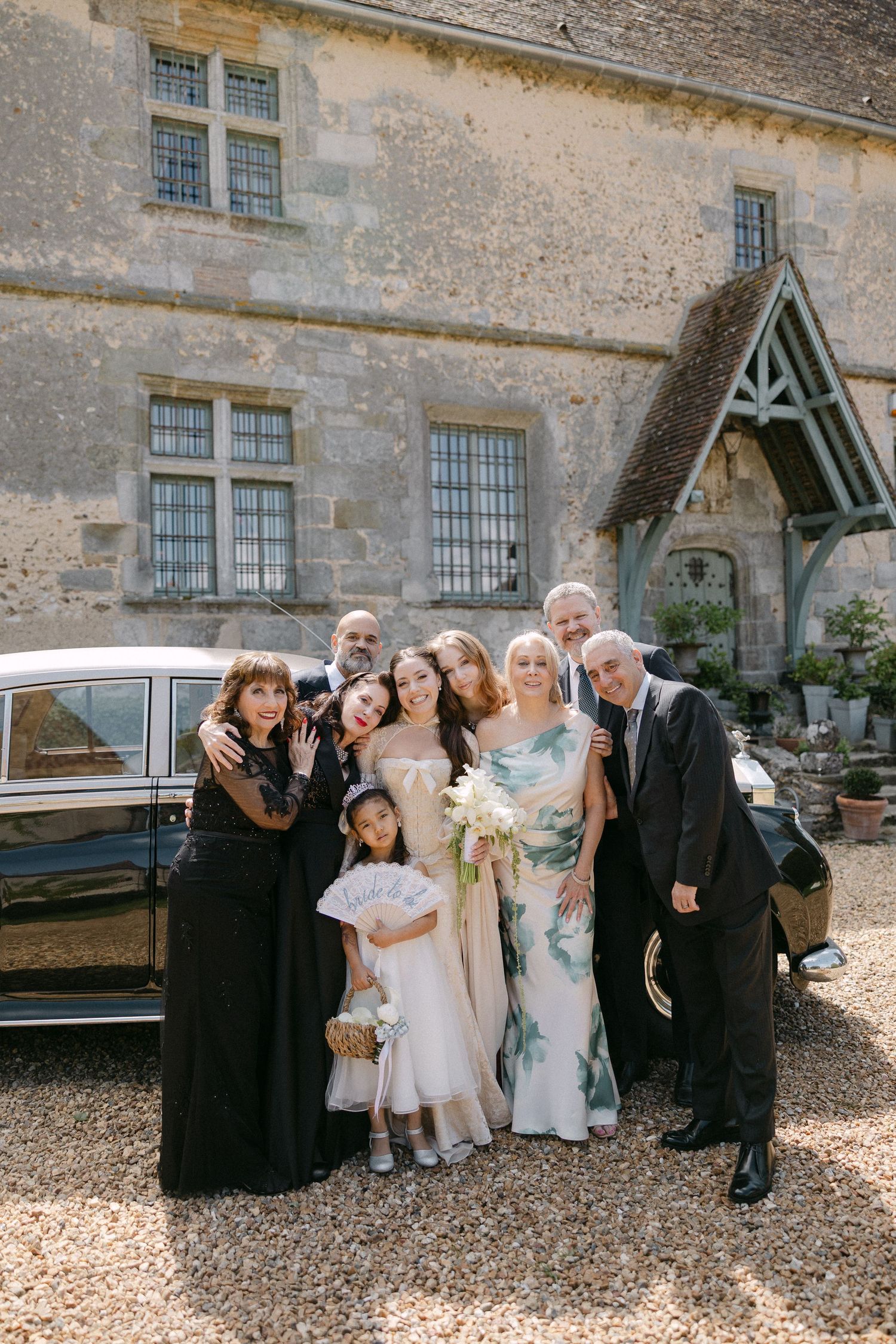 Wedding party group photo outside a historic stone manor with bride in floral dress holding white bouquet.