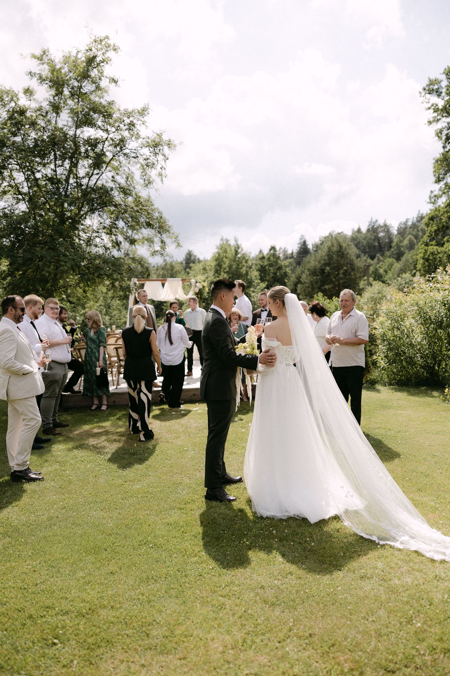 Bride and groom exchanging vows at outdoor wedding ceremony on green lawn surrounded by guests.