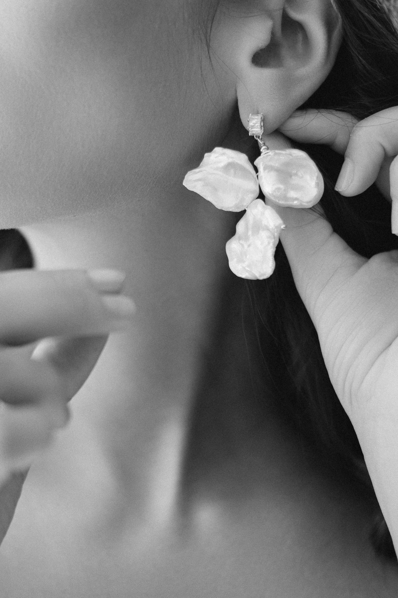 Woman putting on a large baroque pearl drop earring with diamond accent, elegant black and white jewelry photo.
