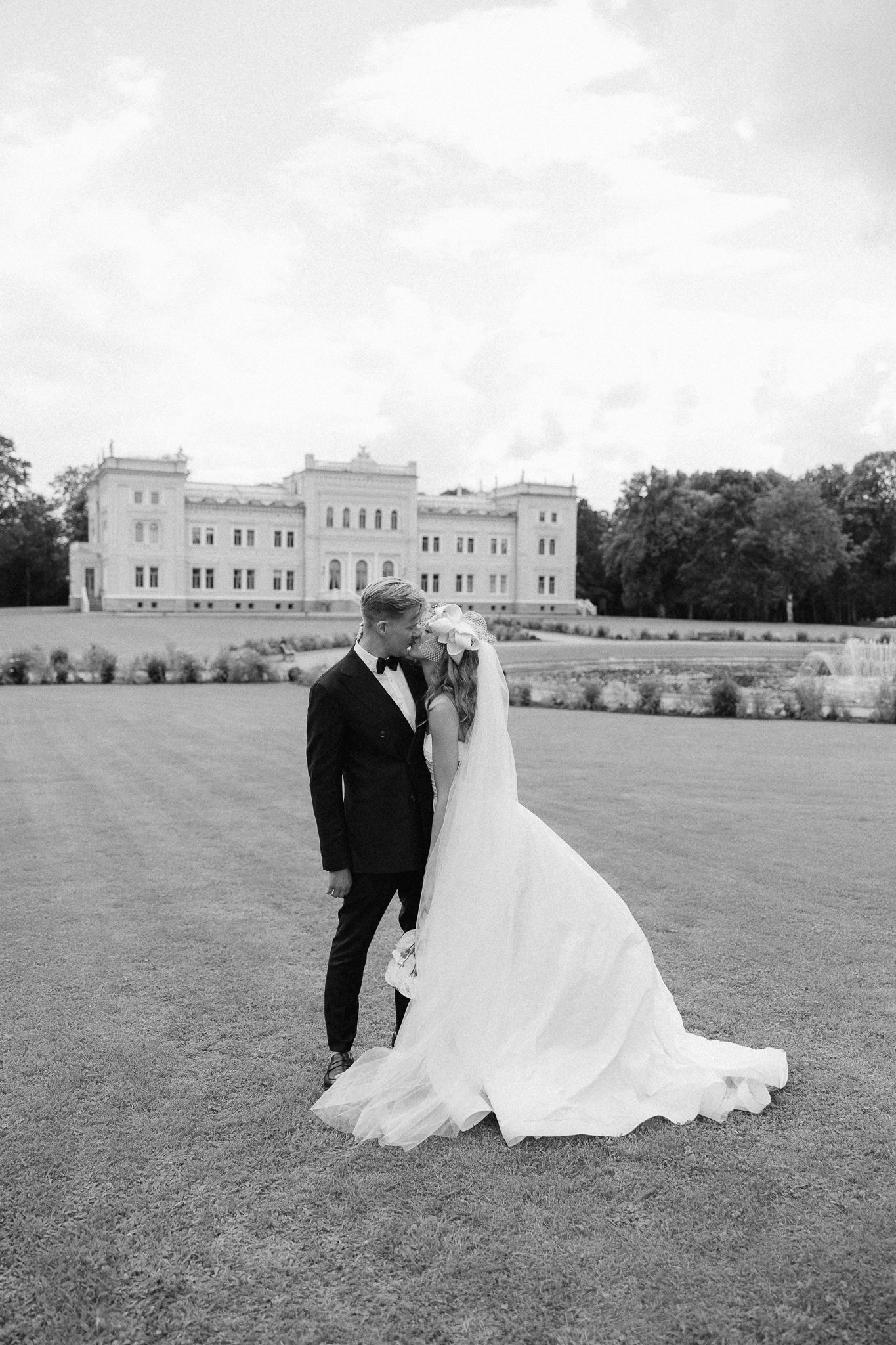 A romantic black and white wedding photo series showing a couple sitting together on a grand lawn with a mansion backdrop.