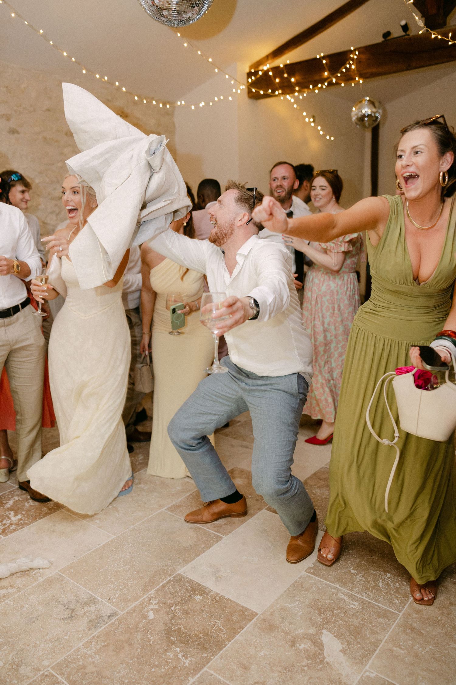 Lively wedding reception dance floor with bride, groom, and guests celebrating joyfully in a rustic stone venue.