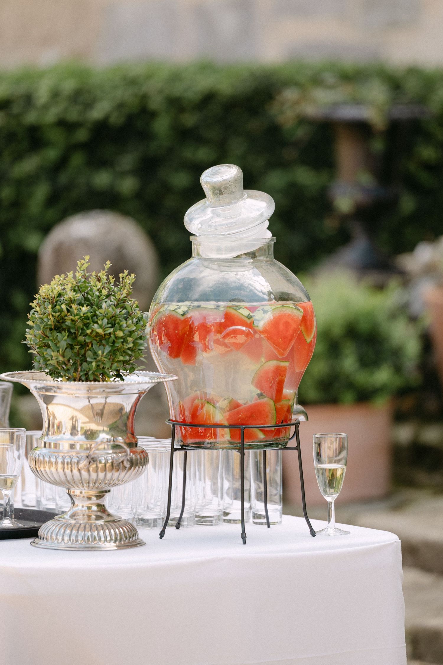 Glass beverage dispenser with strawberries on white tablecloth at an outdoor wedding reception.