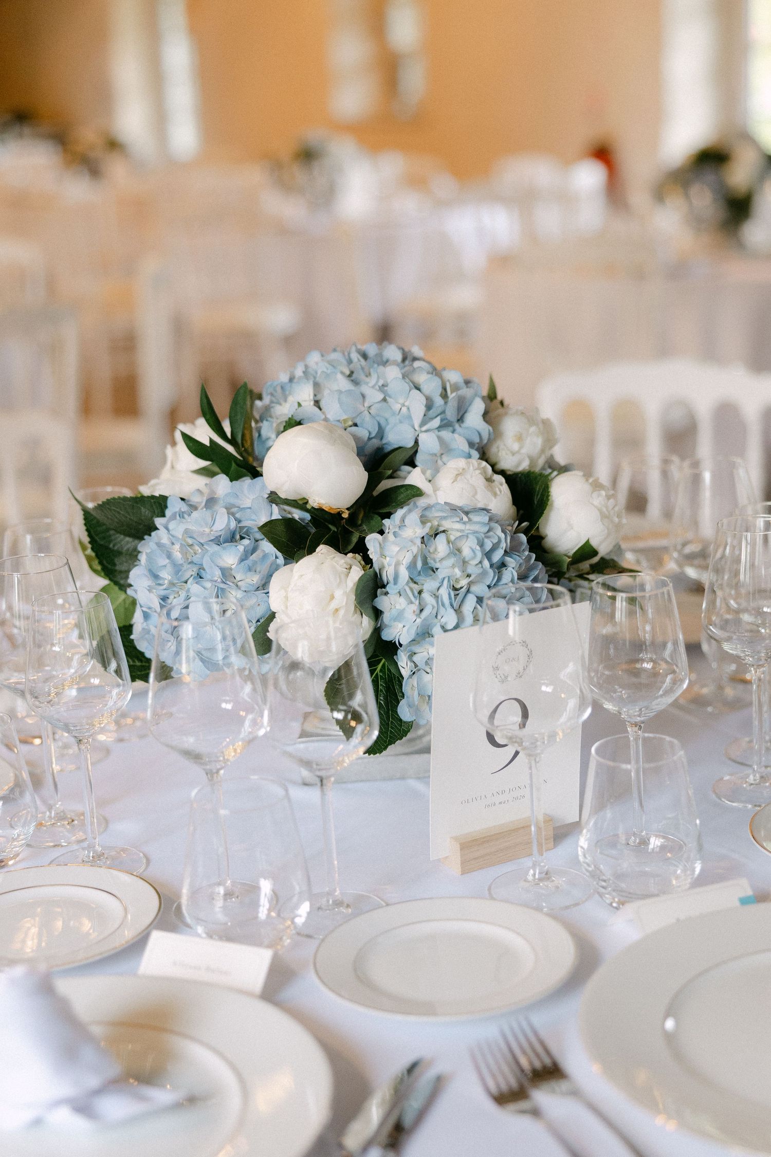 Wedding reception table set with blue hydrangea and white peony centerpiece and crystal glassware.