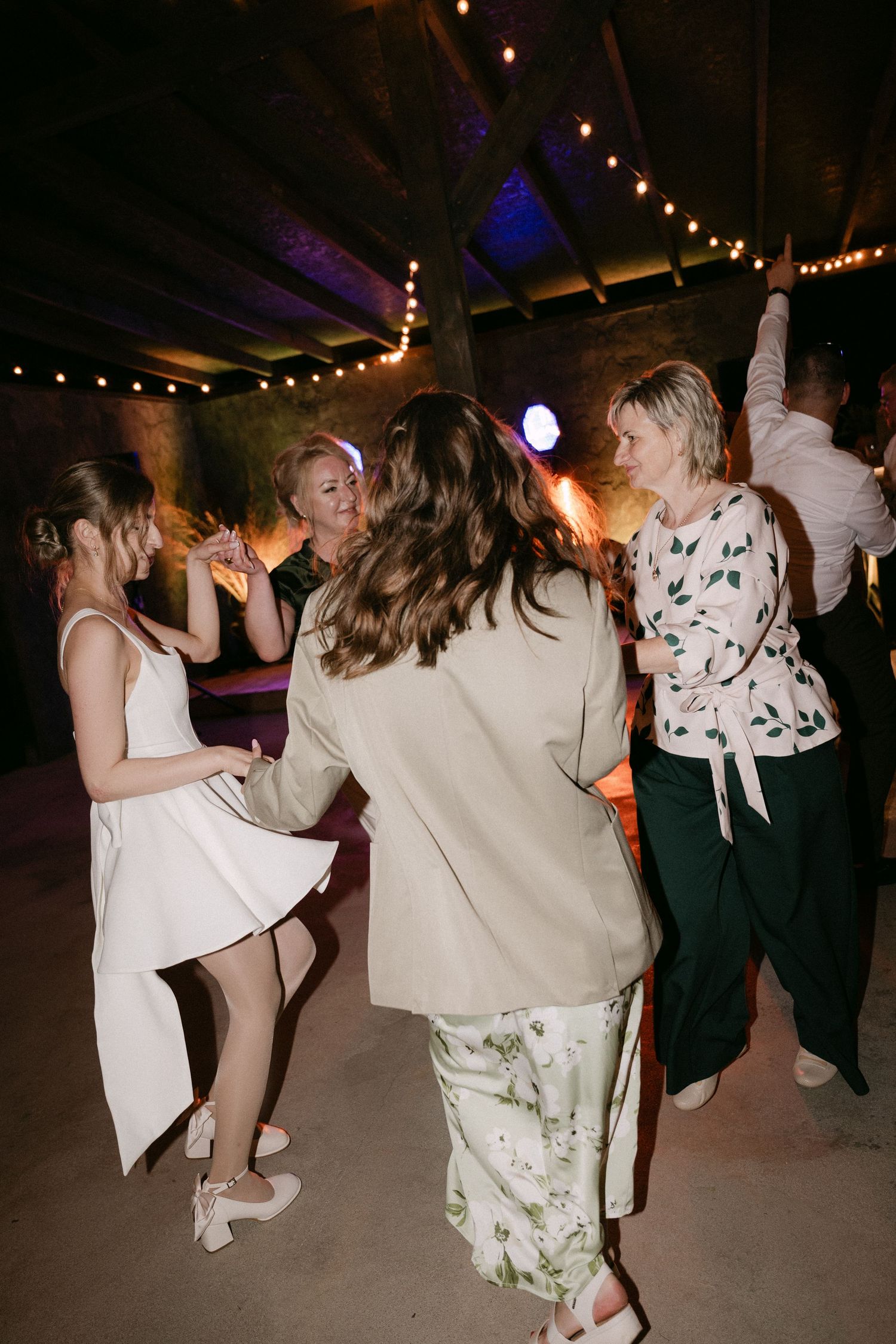 Guests dancing joyfully at an indoor wedding reception with string lights and warm ambiance.