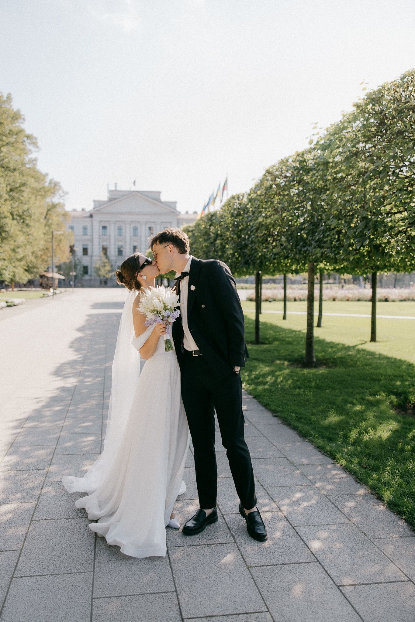 Elegant wedding couple walking along stone pathway near government building.