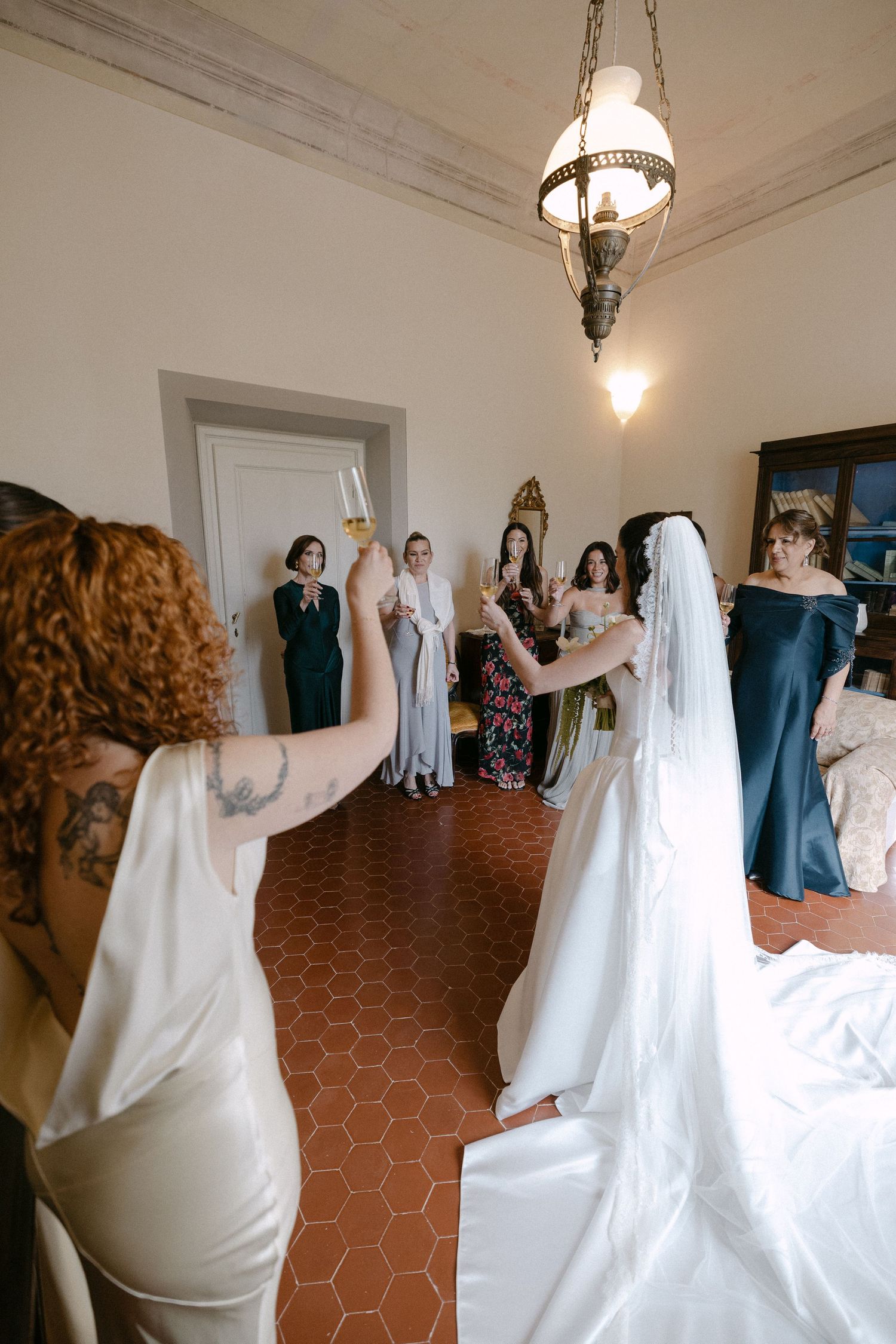 Bride and bridesmaids raising champagne glasses in a toast inside a beautiful Italian villa.