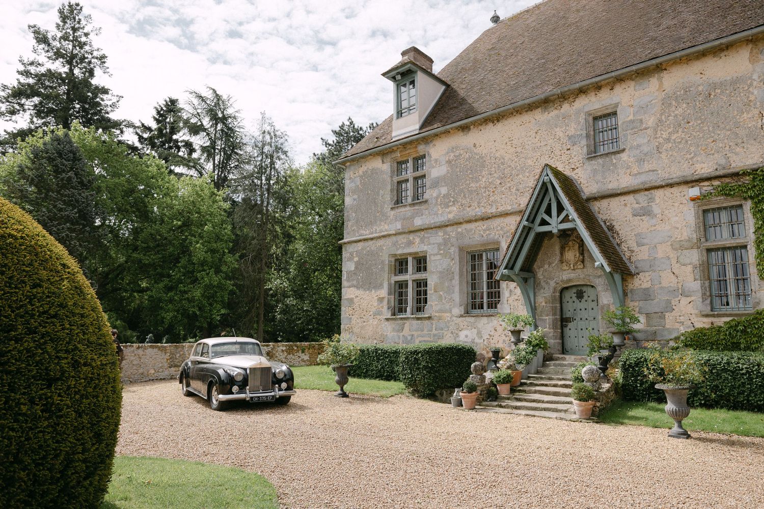 Vintage Rolls-Royce parked outside a charming Cotswolds stone manor house with manicured hedges.