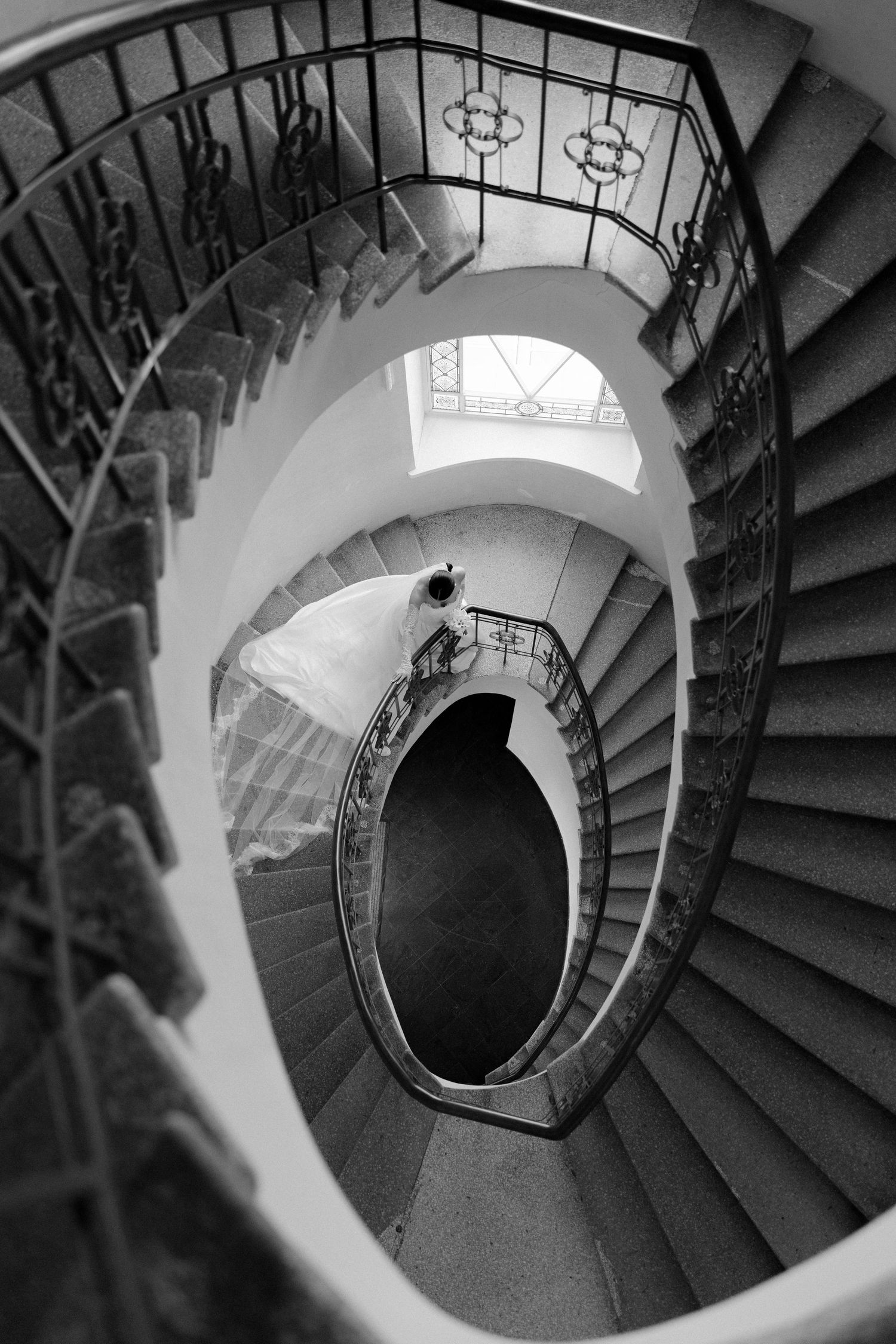 Black and white aerial view of elegant spiral staircase with ornate iron railings in a historic building.