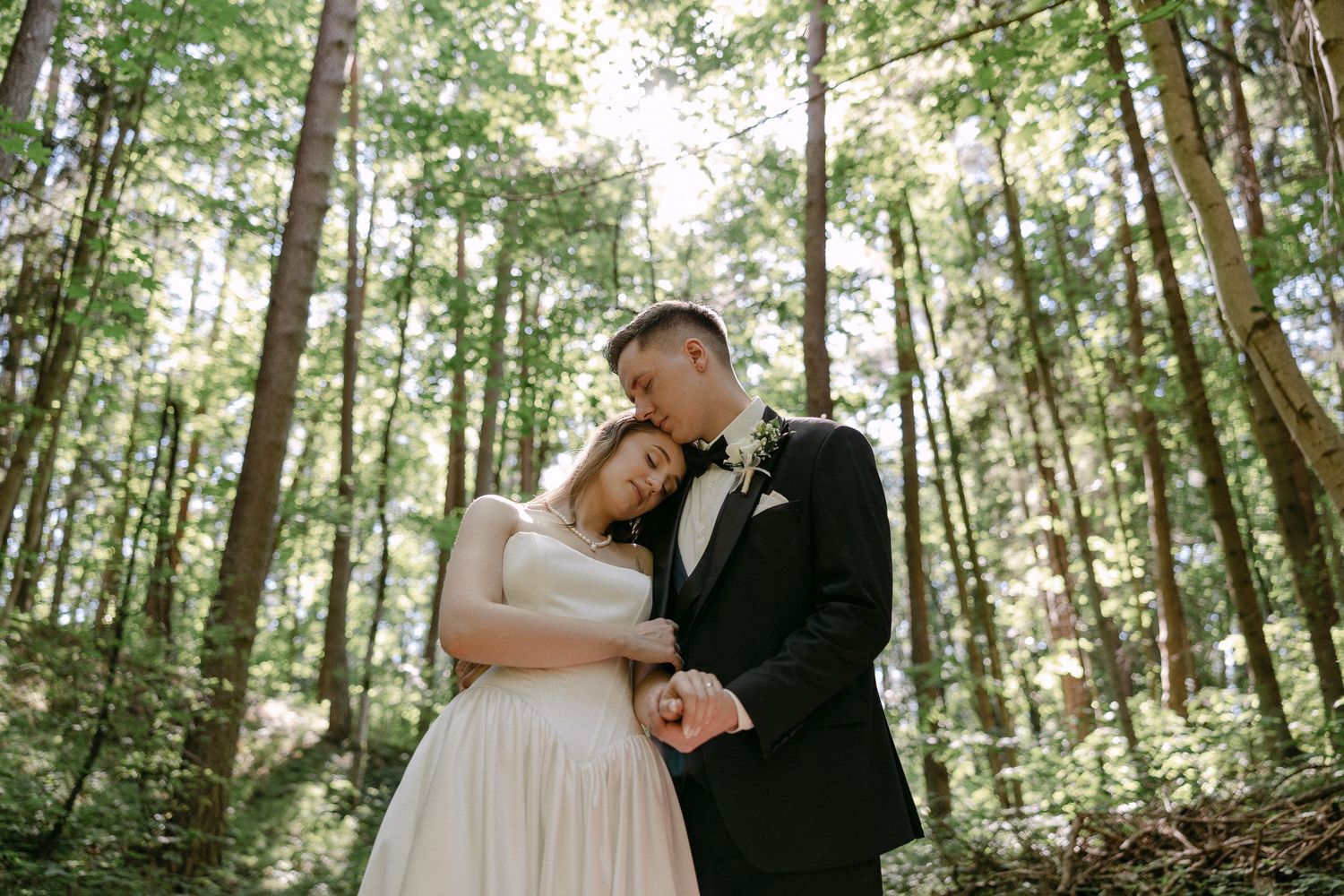 Newlyweds embrace tenderly among tall trees in a lush forest setting.
