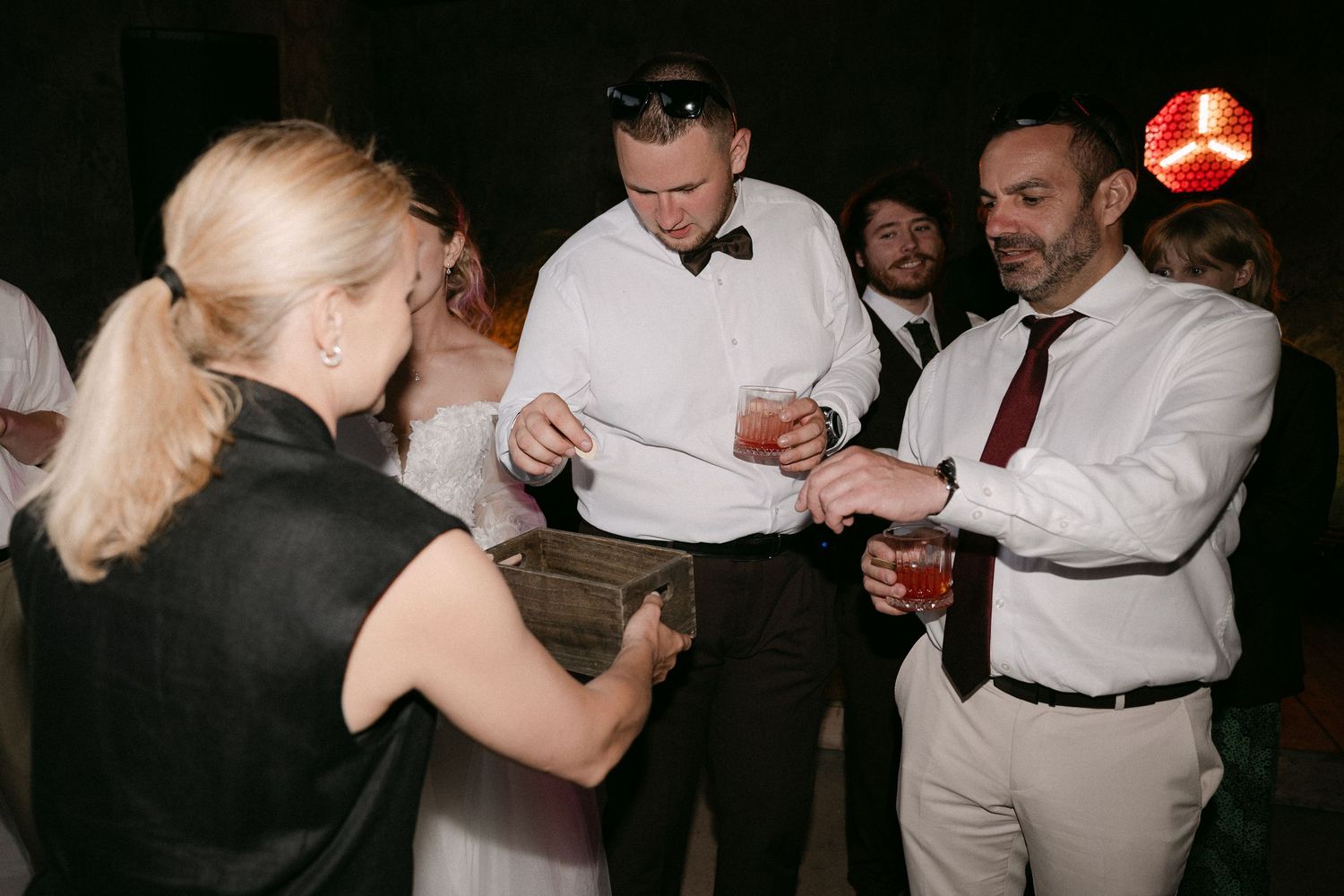 Wedding reception guests dancing and socializing under dim lights during a lively evening celebration.