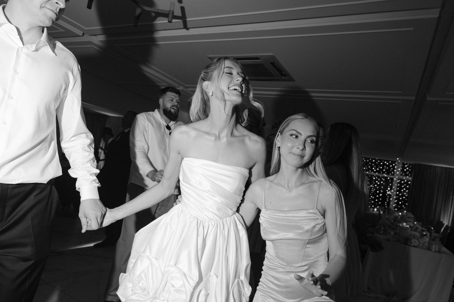 Black and white photo of bride dancing joyfully with guests at a wedding reception.