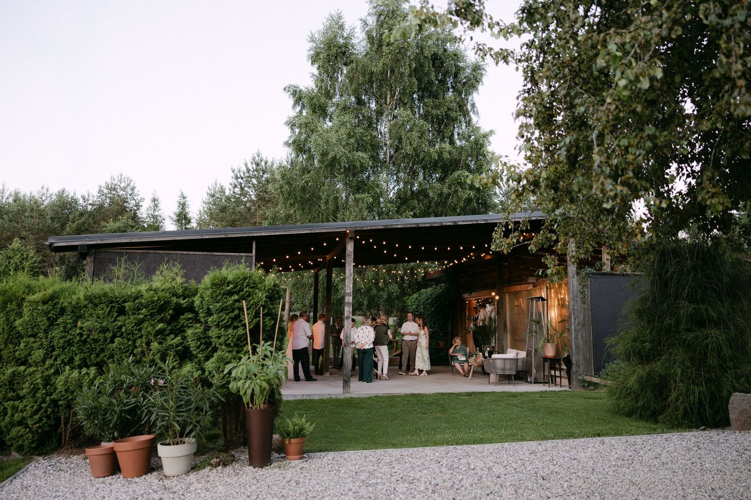Wedding guests mingle under a modern black pavilion with string lights at dusk.