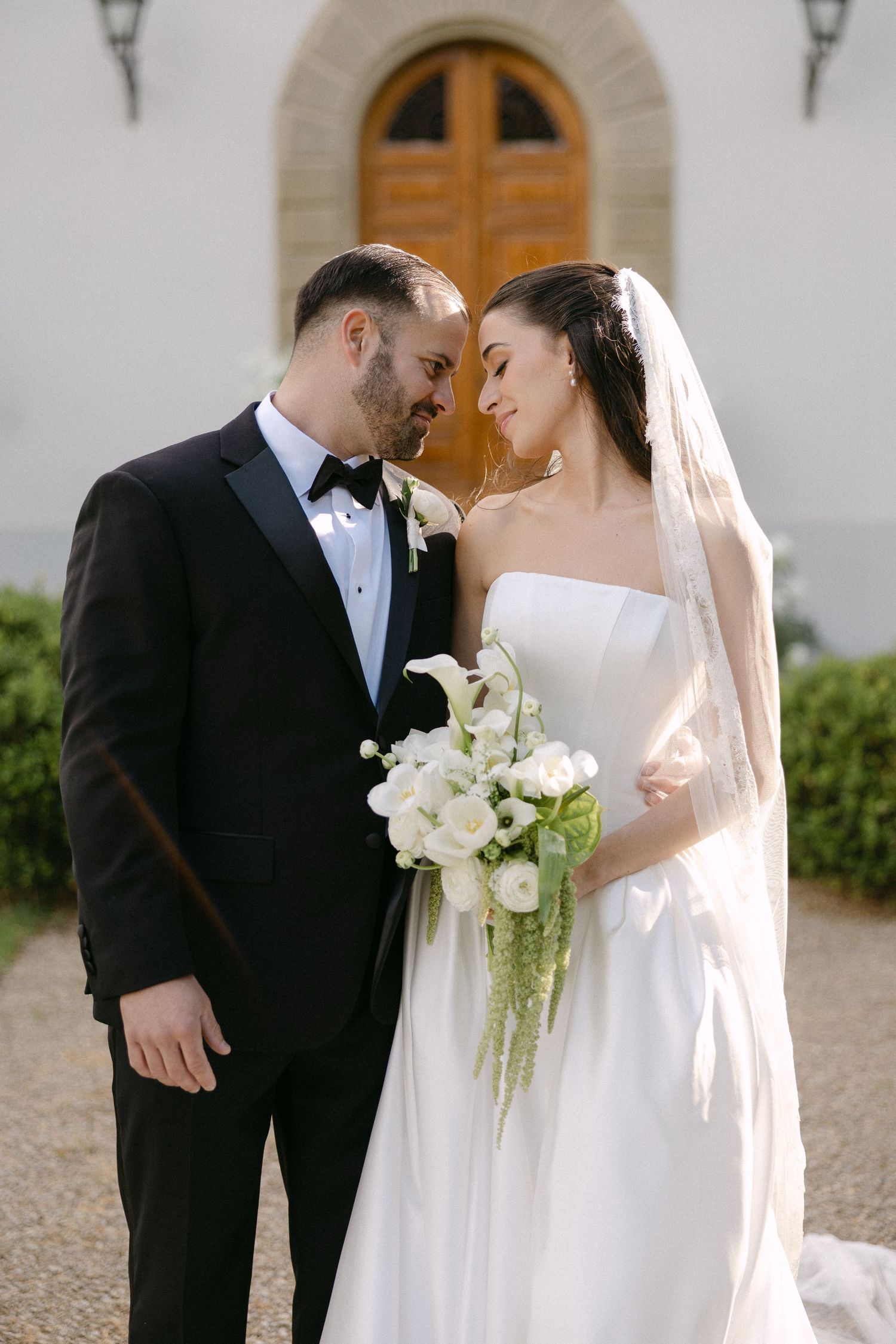 Bride and groom sharing an intimate moment holding a white calla lily bouquet outside a chapel.