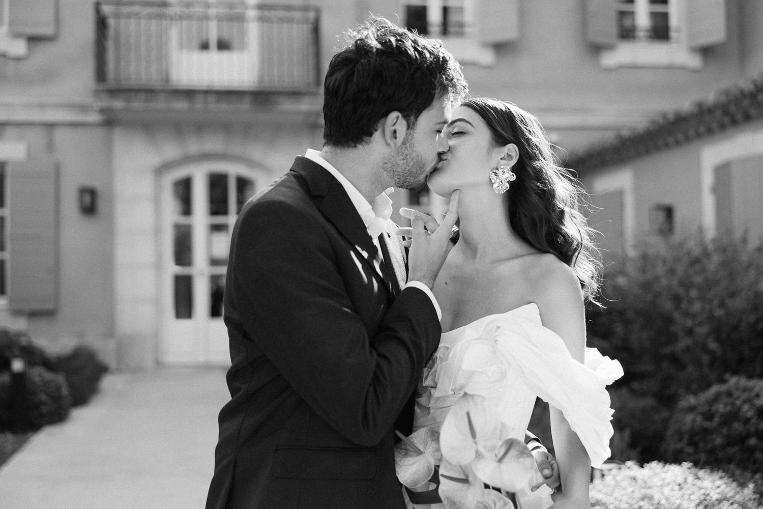 Black and white photo of a couple sharing a romantic kiss on their wedding day outdoors.
