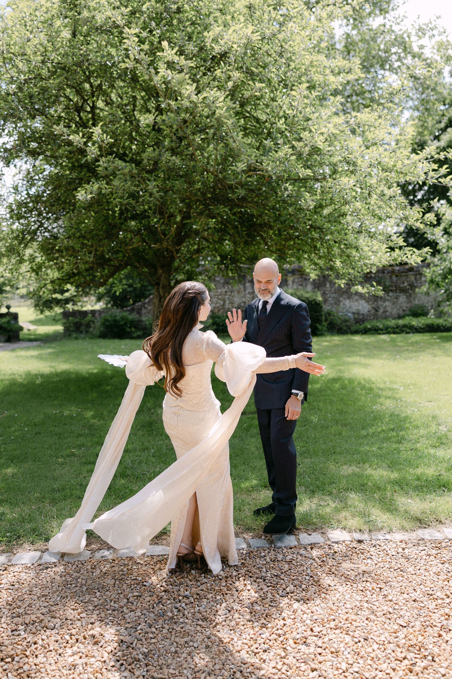Bride in elegant white gown with flowing sleeves doing a first look reveal with groom in garden.
