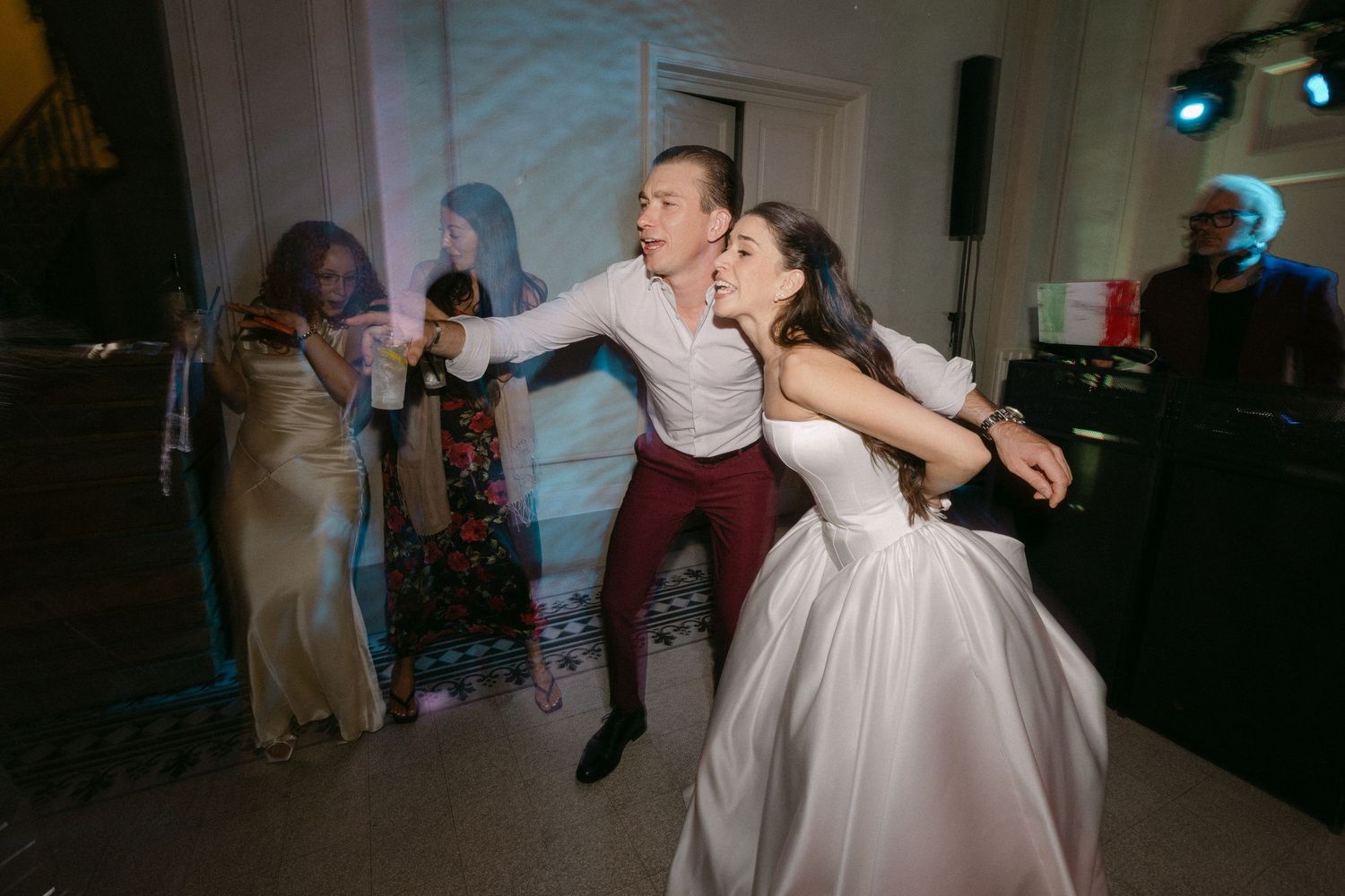 Bride and groom dancing energetically with guests and violinist at lively wedding reception.