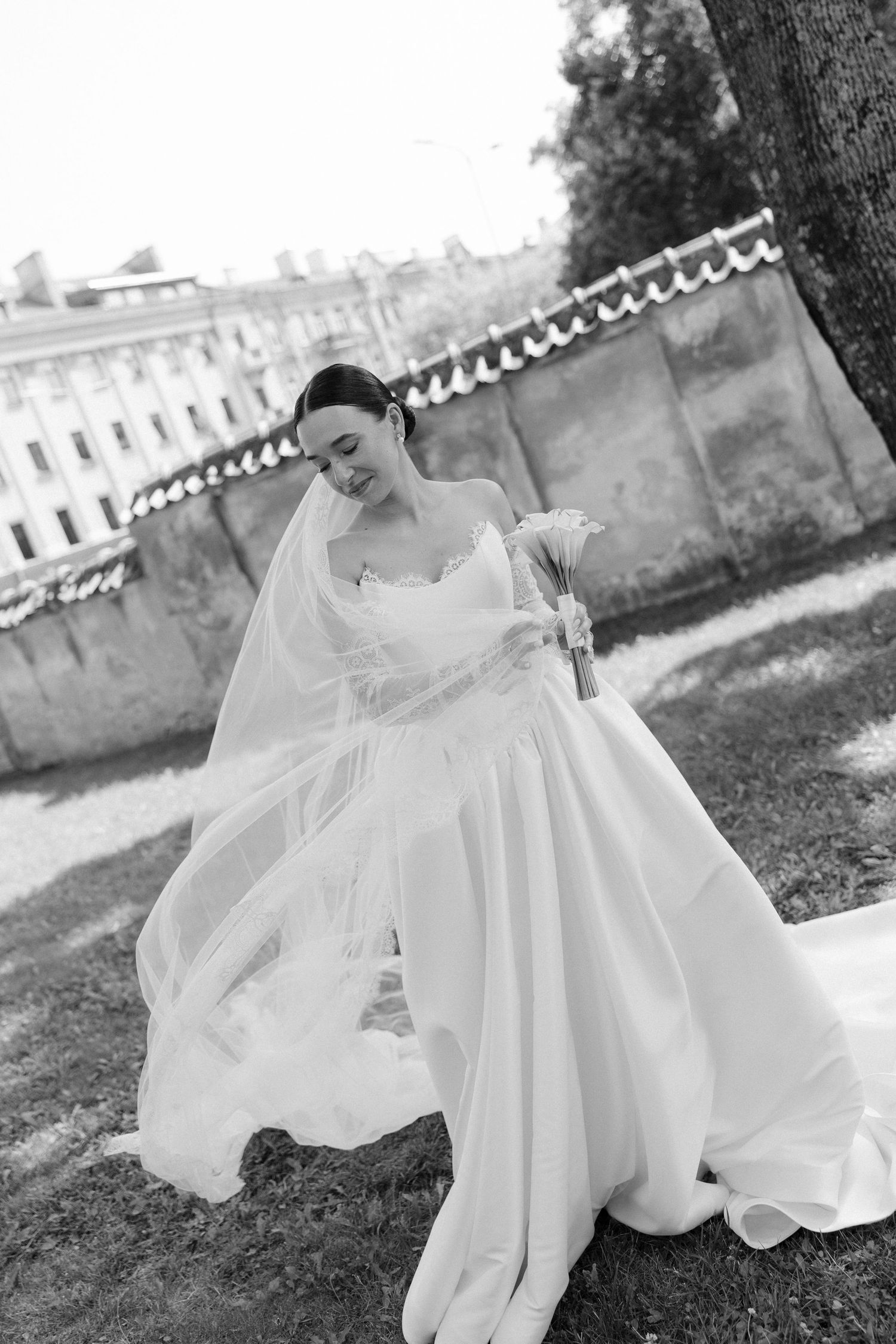 Black and white photo of bride in flowing white gown and veil posing outdoors.