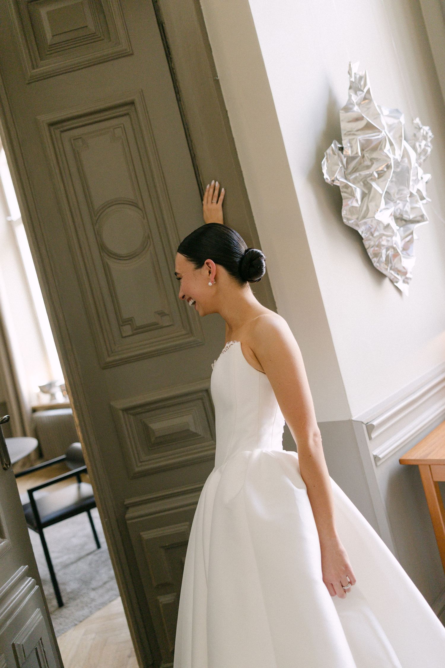 Beautiful bride in a strapless white wedding gown laughing while opening an ornate door in a elegant room.