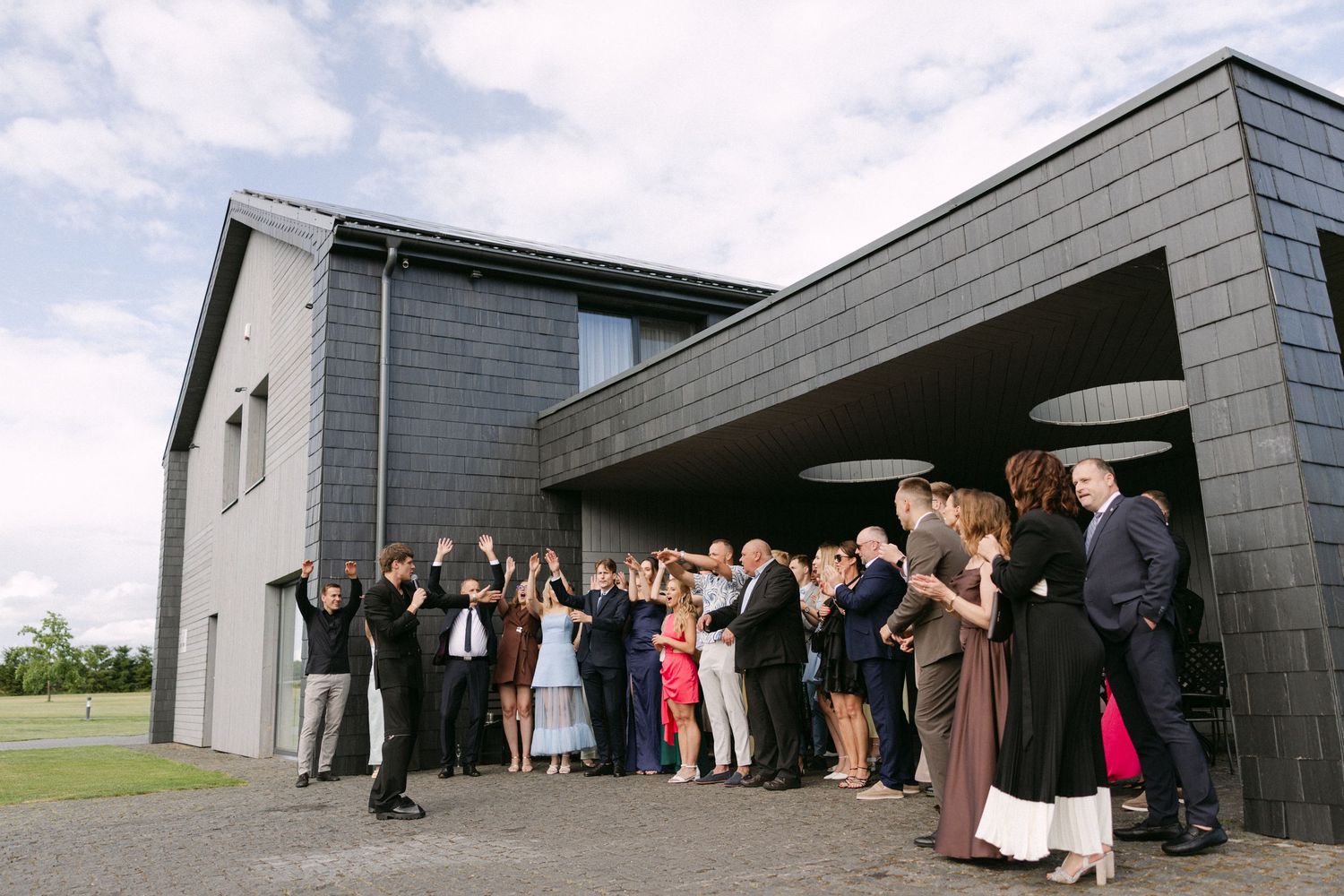 Wedding guests gathered outside a modern dark slate building celebrating after a ceremony outdoors.