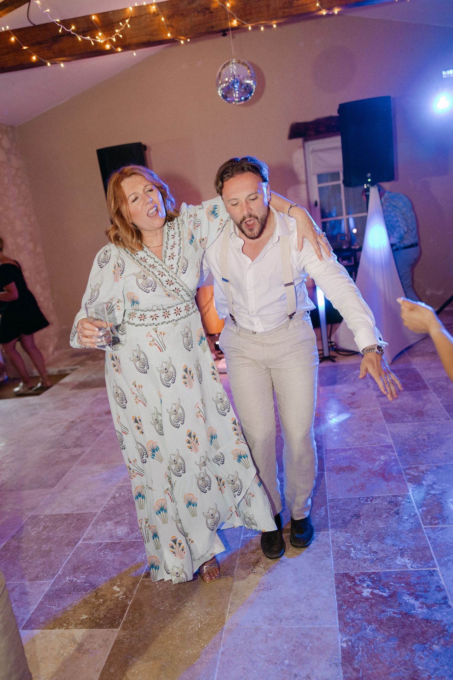 Groom in white shirt dancing energetically with older woman guest at fun wedding reception.