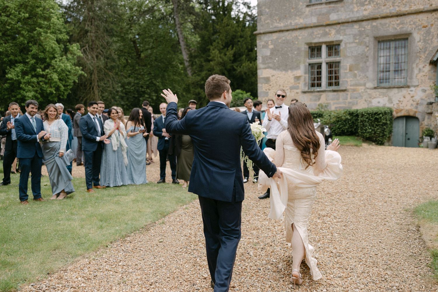 Newlywed couple walking triumphantly toward guests gathered outside a historic stone wedding venue.