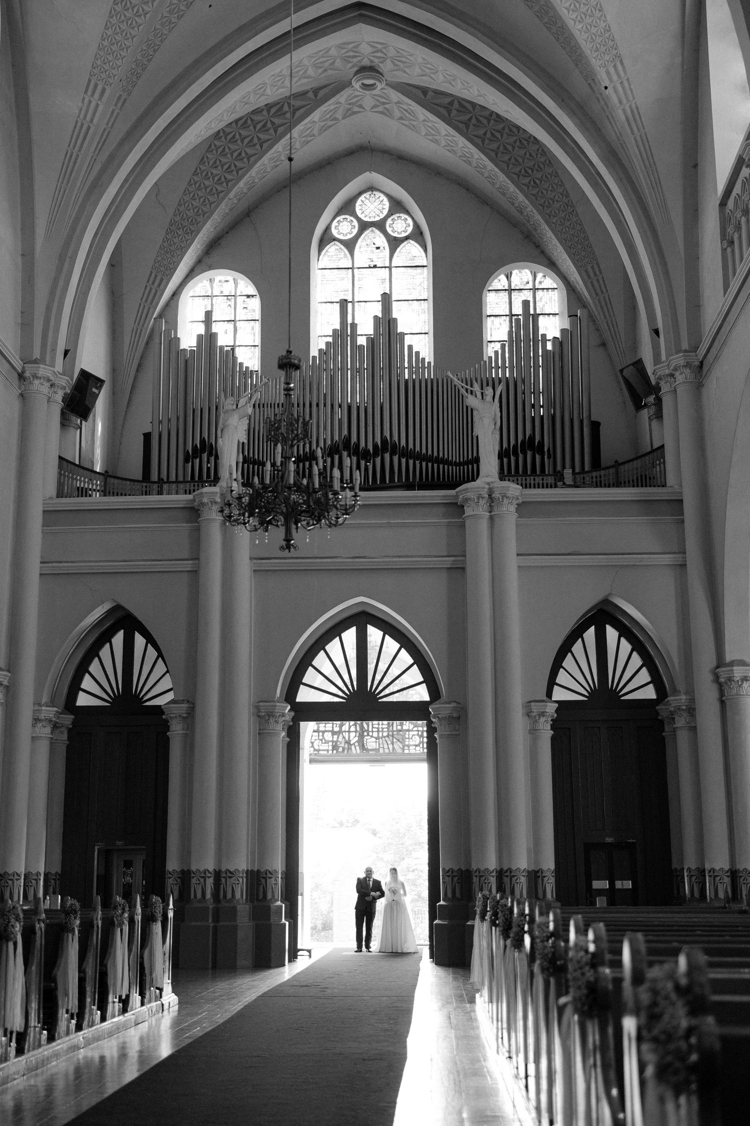 Black and white photo of bride and groom silhouetted in grand cathedral doorway with pipe organ above.