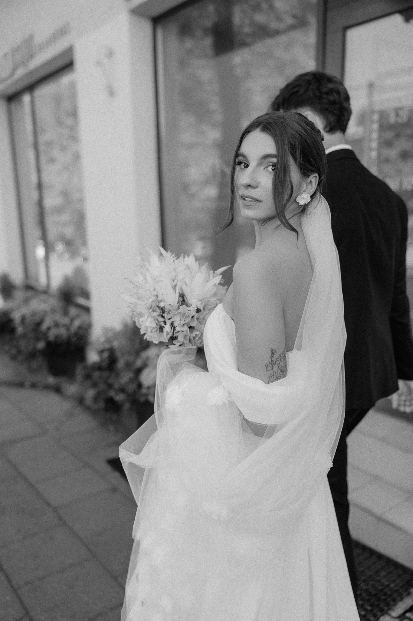 Bride in flowing white dress holding bouquet while standing outside.