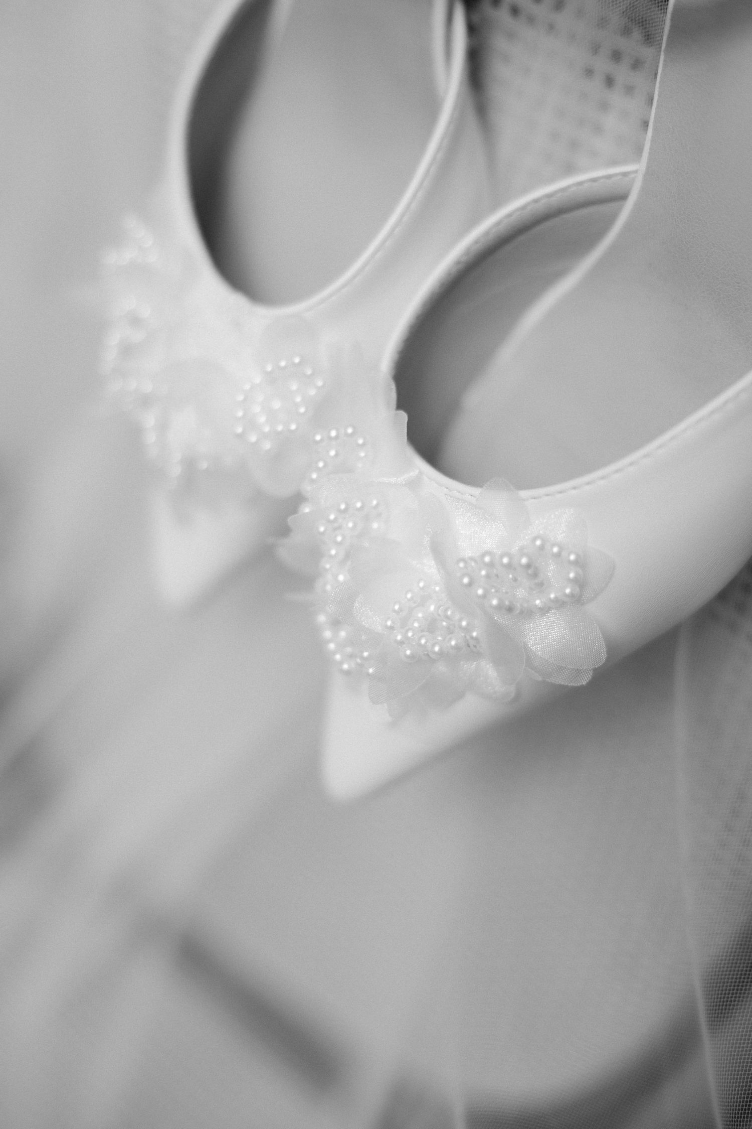 Close-up black and white photo of bridal shoes adorned with delicate pearl and floral embellishments.