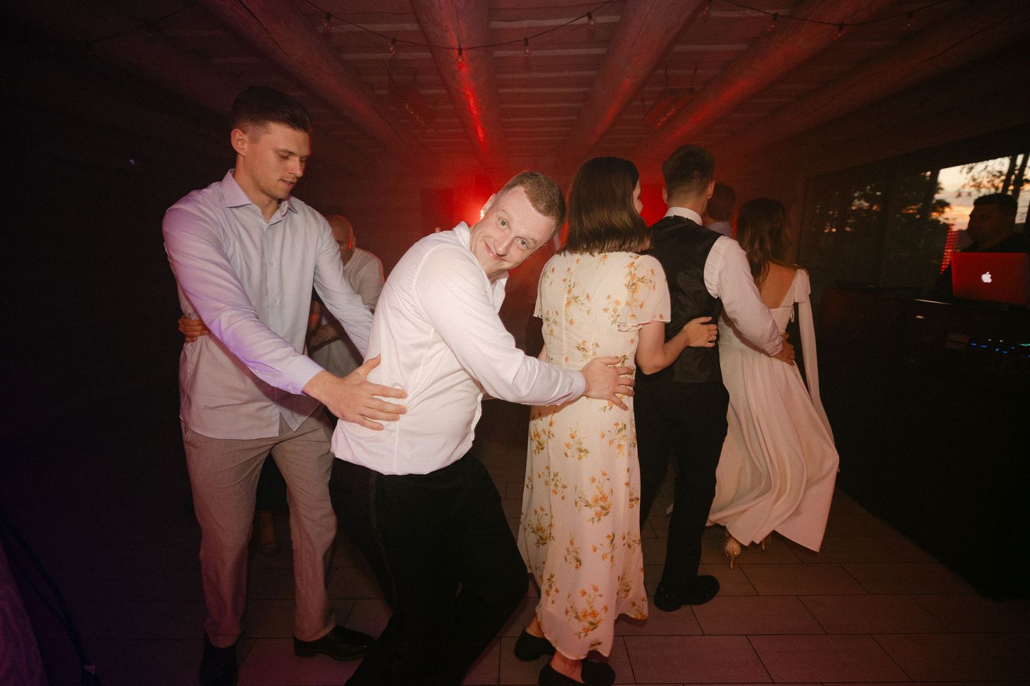 Guests dancing joyfully under red lights at lively wedding reception party.