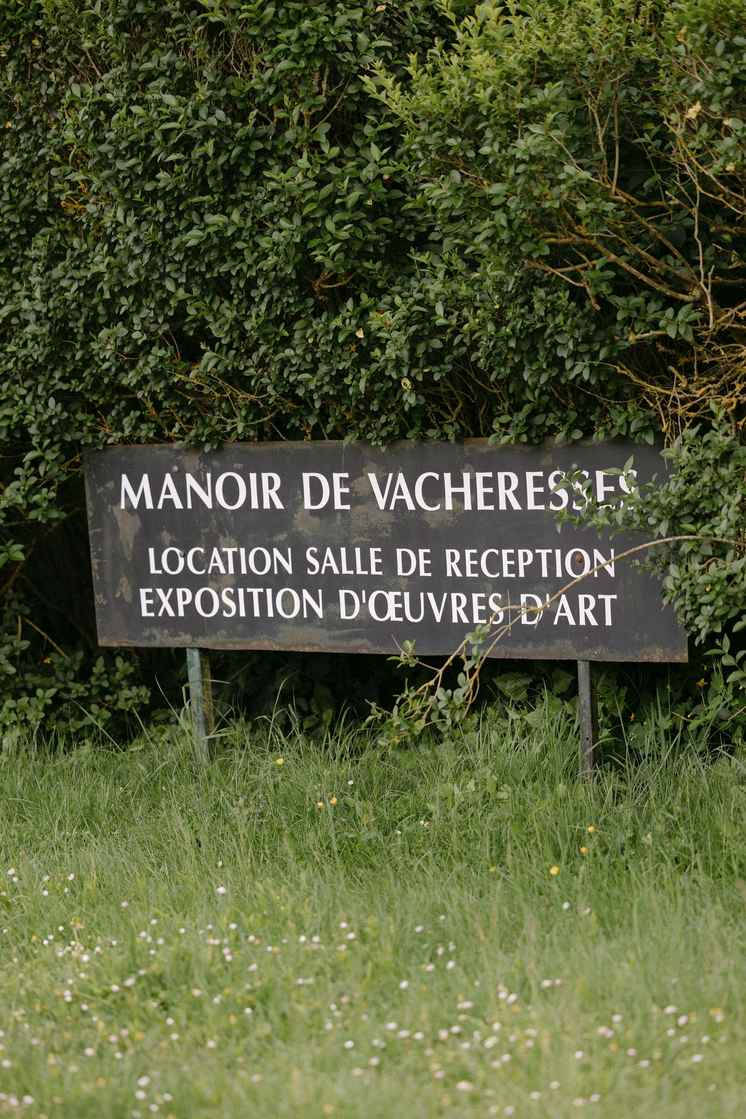 Black sign for Manoir de Vacheresses advertising reception hall rental and art exhibition in French countryside.