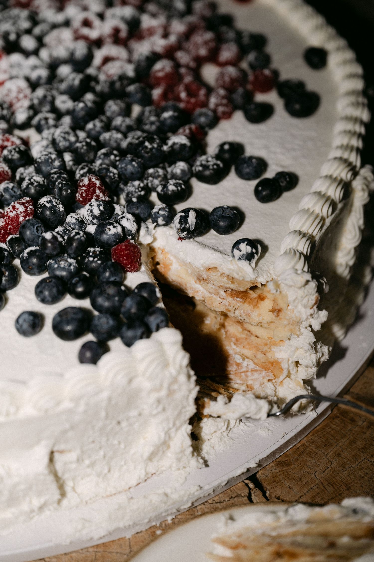 White wedding cake topped with fresh blueberries and raspberries dusted with powdered sugar, with a slice removed.