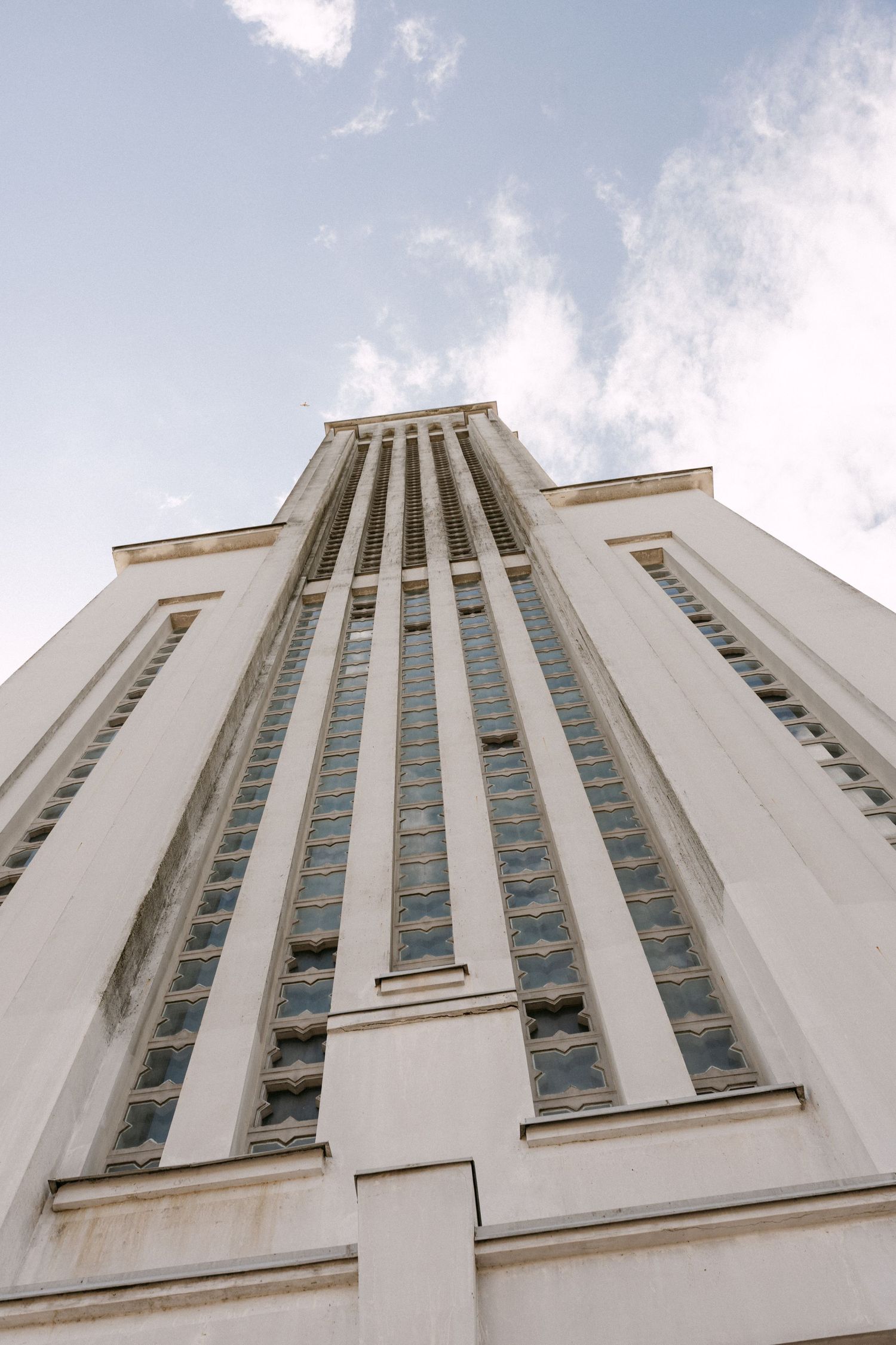 Low angle view of a tall Art Deco white building with large stained glass windows against cloudy sky.