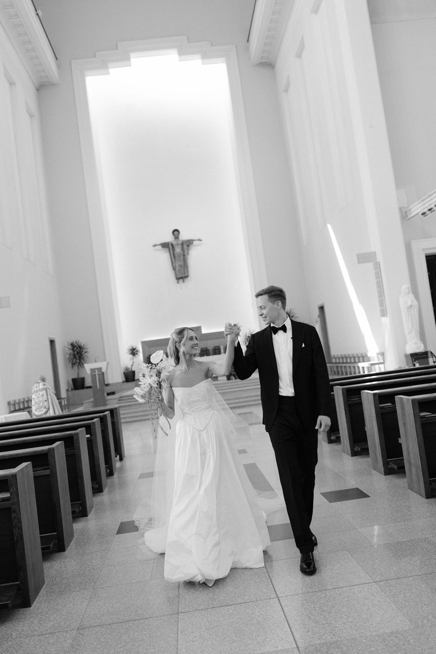 Black and white photo of a bride and groom holding hands walking down the aisle of a church after their wedding ceremony.