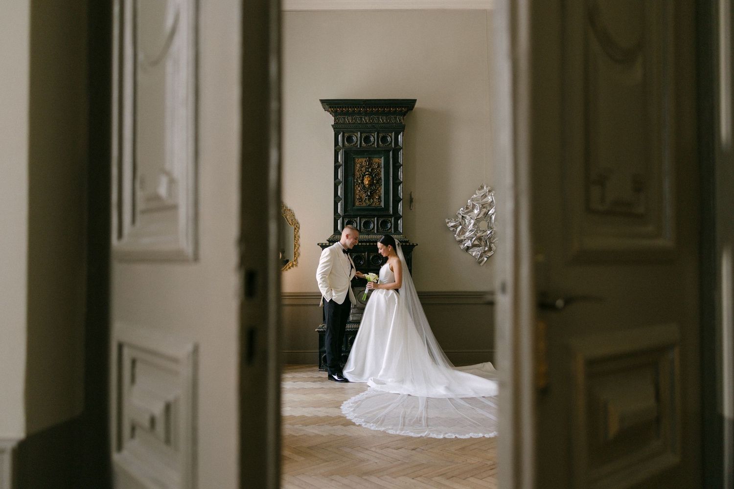Bride and groom share an intimate moment in an elegant villa hallway, framed by ornate doors, with a flowing white wedding gown.
