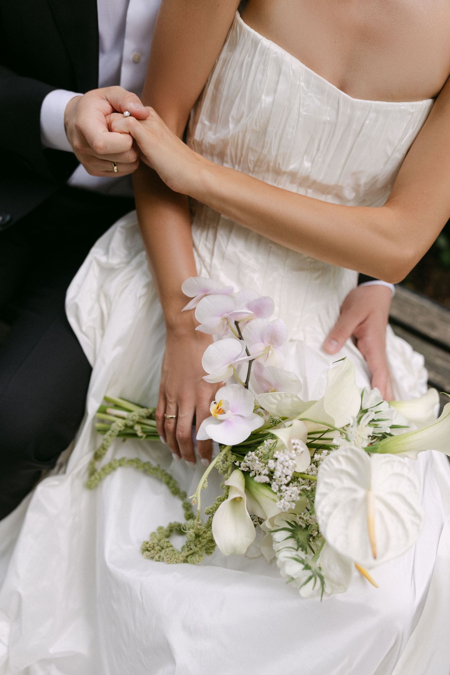 Close-up of bride and groom holding hands with an elegant white orchid and calla lily wedding bouquet.