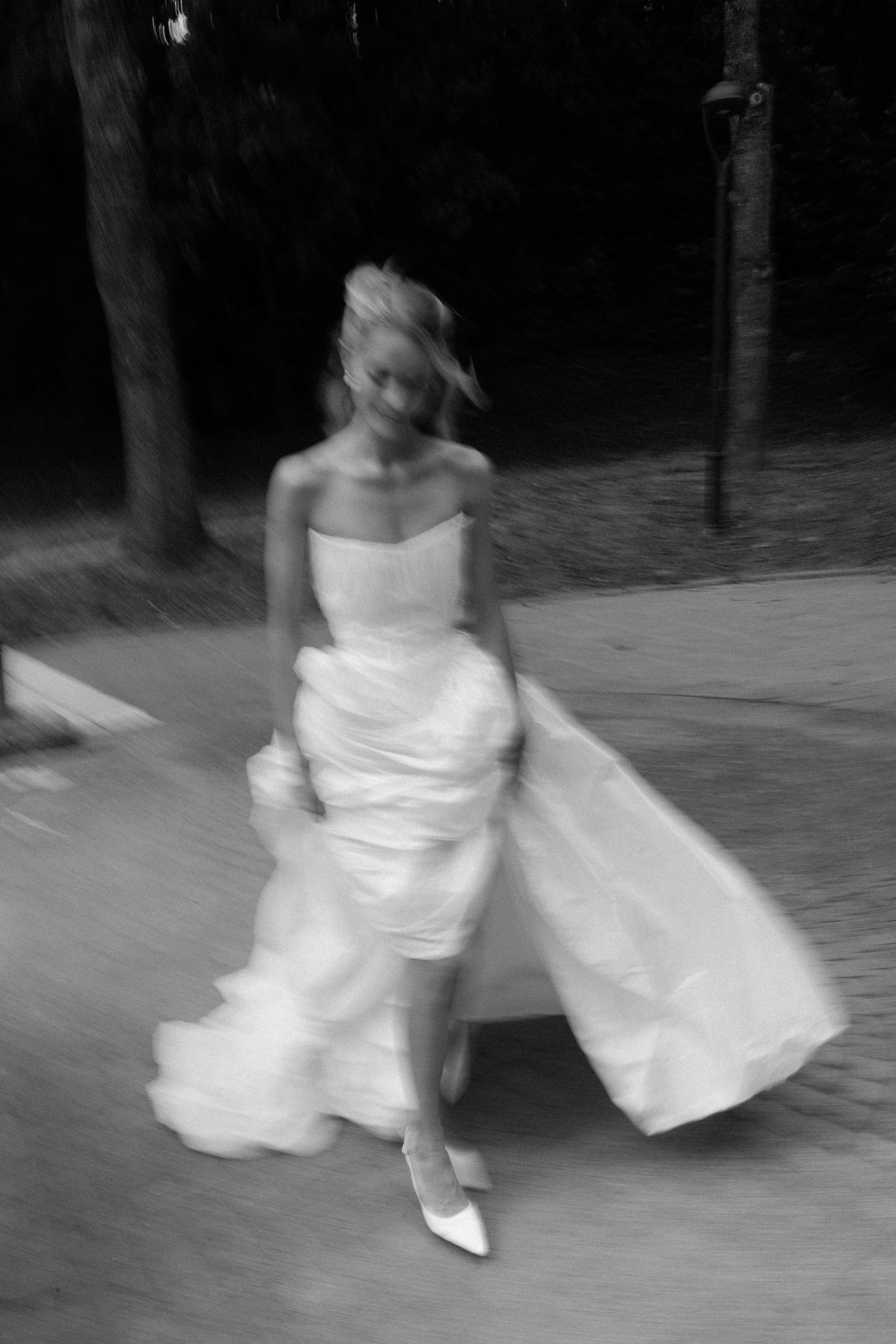 Artistic blurred black and white photo of bride in white gown running through wooded path.