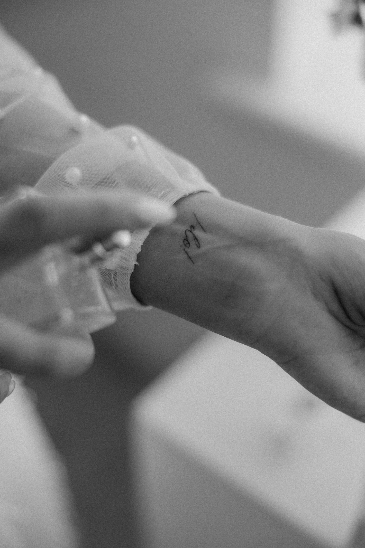 Black and white close-up of delicate lace sleeve and small wrist tattoo.